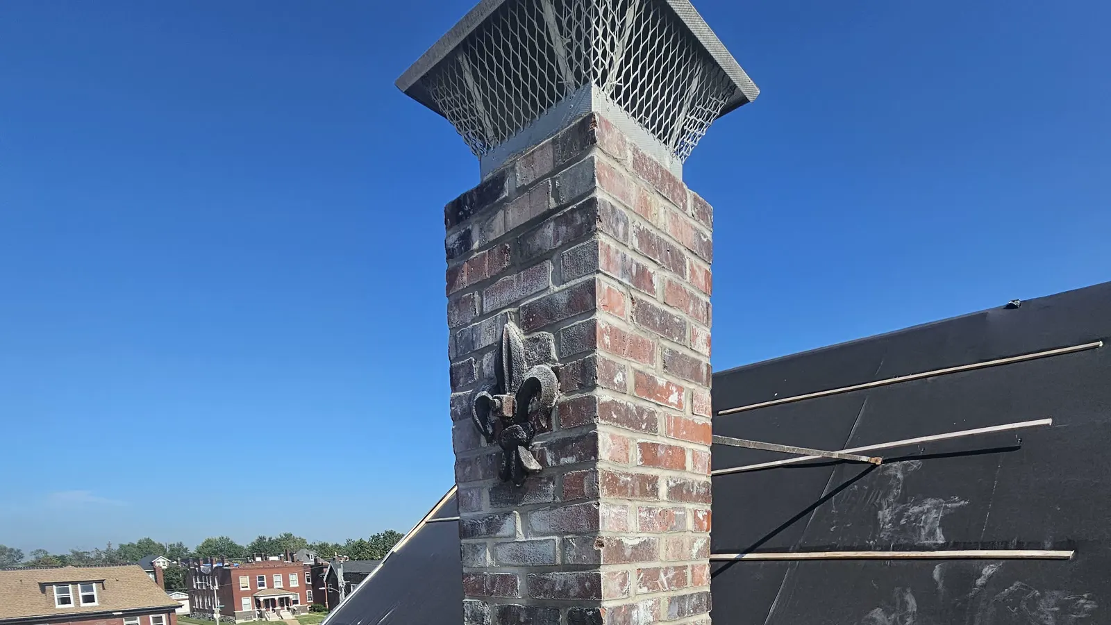 A chimney Billy rebuilt: fresh multi-tone brick, clean struck joints, a new cap, and the fleur-de-lis ornament on the face.