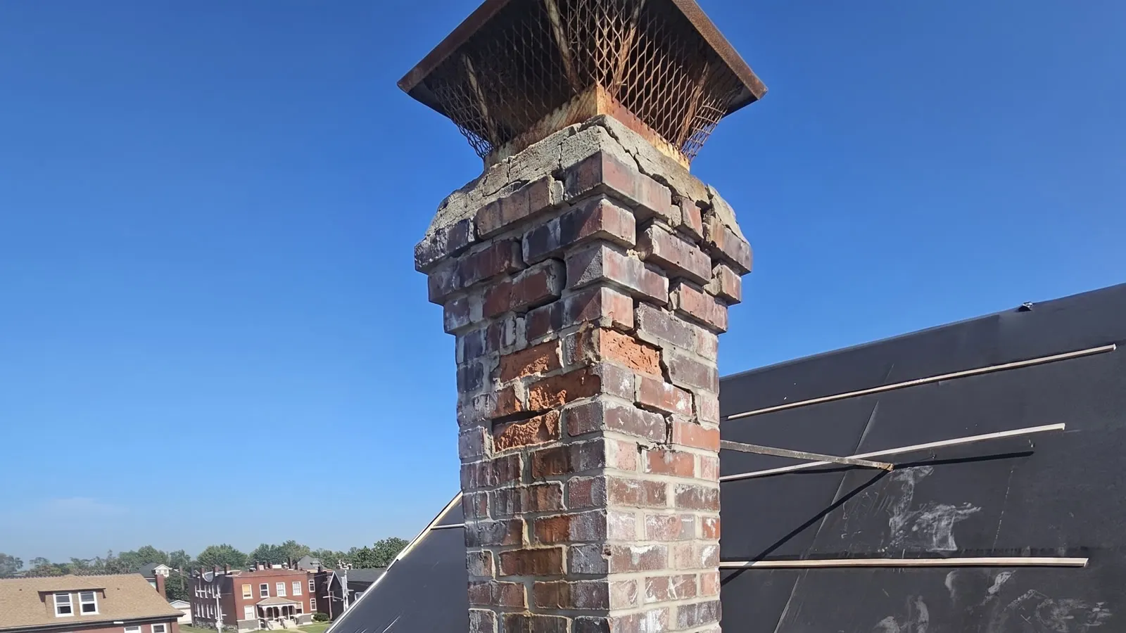 The chimney shown weathered and failing: cracked crown, spalled brick faces, open joints and a rusted cap.