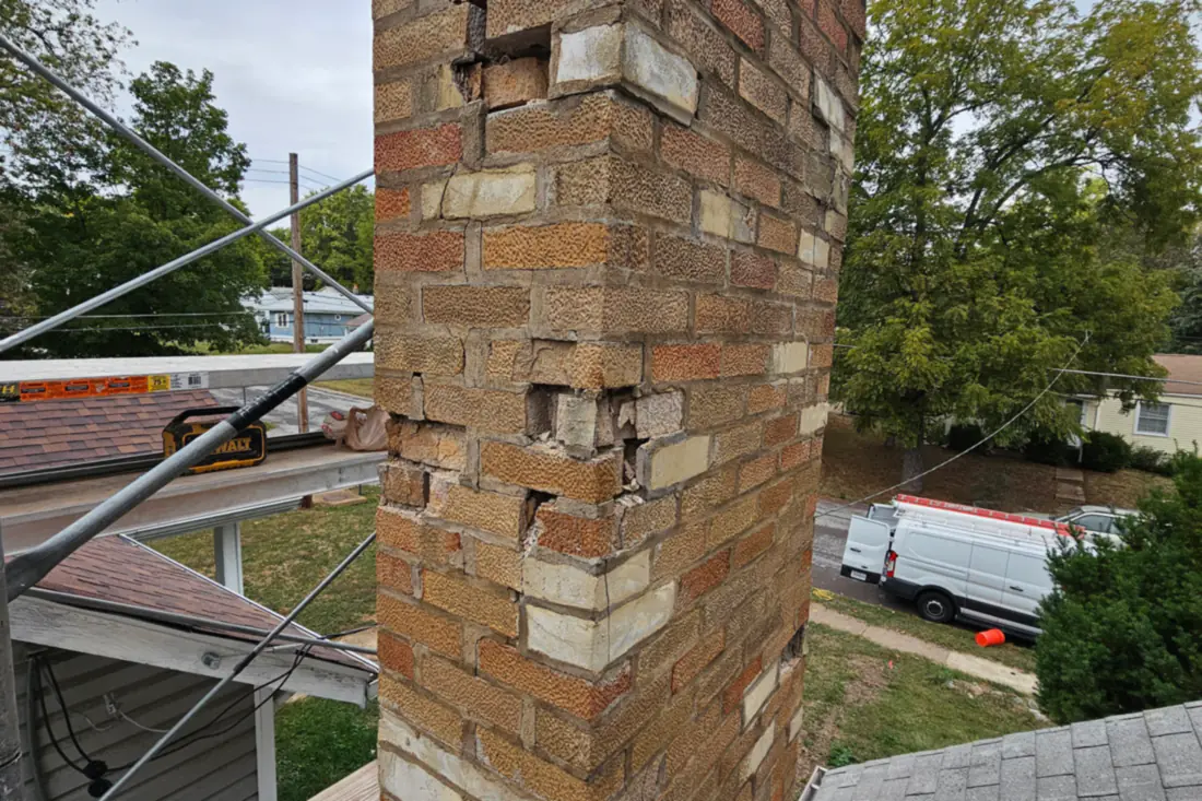 A brick chimney stack with the faces spalled off and the mortar joints washed open near the top.