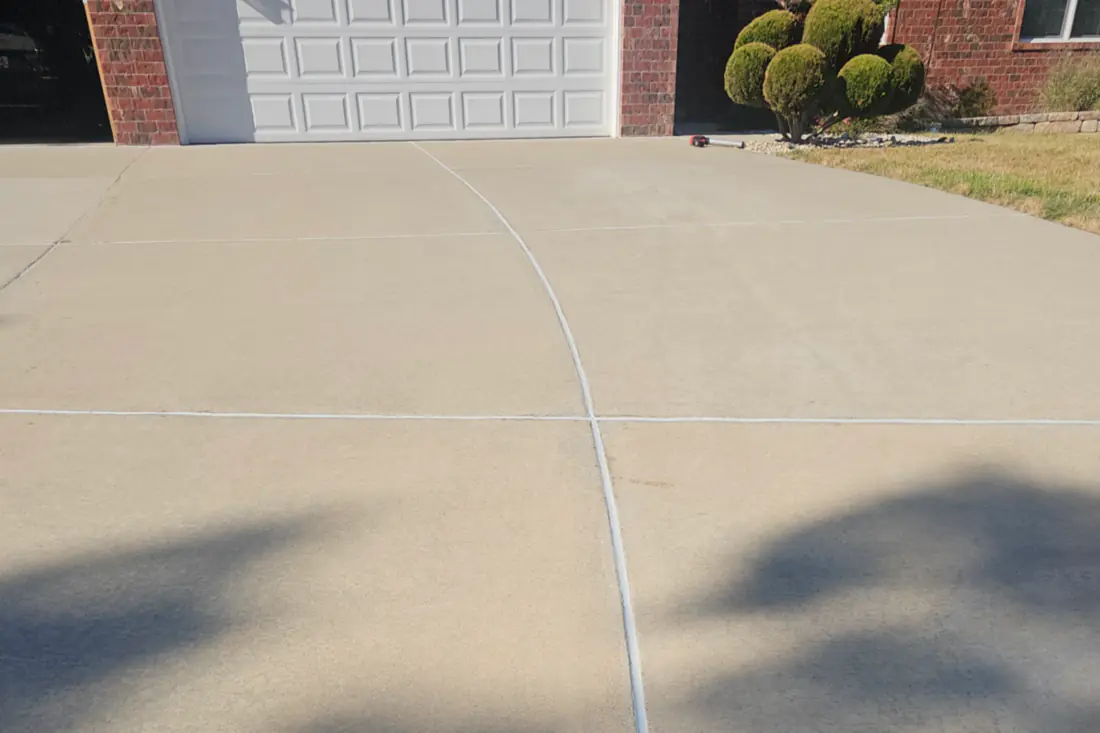 A concrete driveway finished flat and pitched away from the garage, with the control joint cut down the middle.