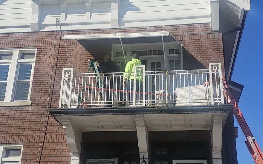 Masonry work underway on the balcony of a two story brick building, with the lift set alongside.
