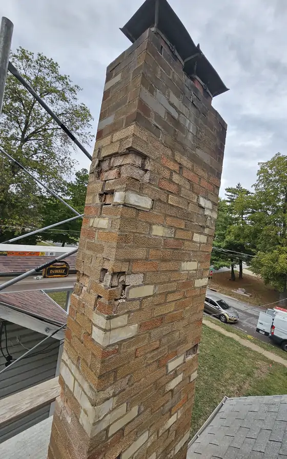 A tall brick chimney with the faces flaked off and the joints washed open, seen from the roof.