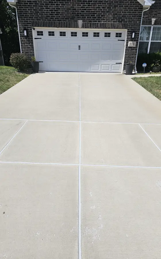A concrete driveway run up to a two car garage, joints cut straight and the edges clean.