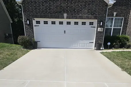 A concrete driveway run up to a two car garage, joints cut straight and the edges clean.