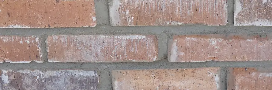 Close up of fresh mortar joints run between mixed tone brick and tooled flush with the face.