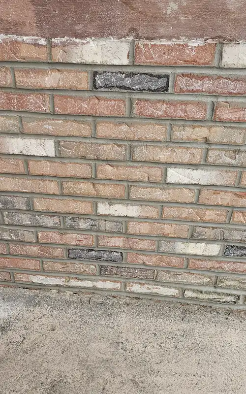 A foundation height brick wall repointed with fresh mortar, the dark header courses picked back out.