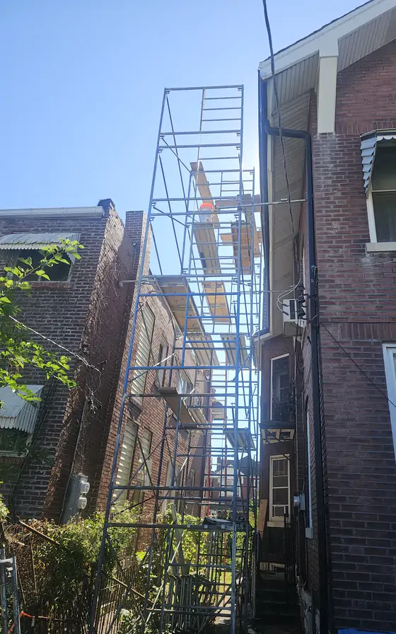 Scaffold stacked up the side of a brick building to reach the upper courses.