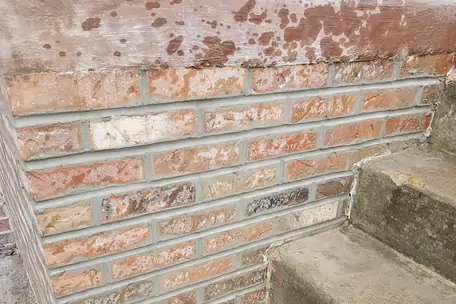A brick wall repointed course by course where it runs alongside a flight of concrete steps.